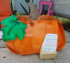 a pumpkin shaped planter sitting on the side of a road with a sign attached to it