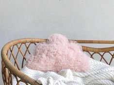 a pink stuffed animal laying on top of a blanket in a wicker basket next to a white wall