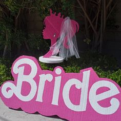 a pink sign that says bride with a veil on it's head in front of some bushes