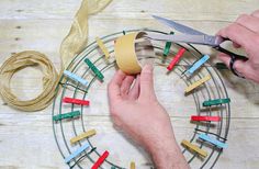 someone is making a wreath out of clothes pins and tape on a wooden table with scissors