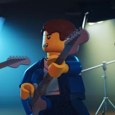 a lego man holding a guitar in front of a microphone and sound equipment on a stage