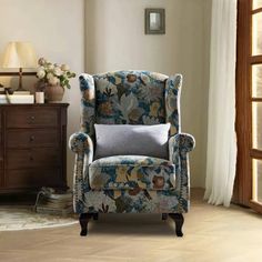 a blue chair sitting in front of a window next to a wooden dresser and lamp