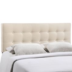 a bed with white linens and pillows on it's headboard, in front of a white wall