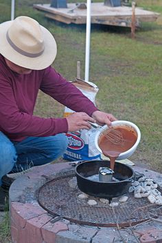 a man in a hat is cooking something on an open fire pit