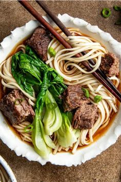 a bowl filled with meat and noodles next to chopsticks on top of a table