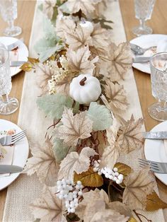 the table is set with plates and silverware, napkins and pumpkins on it