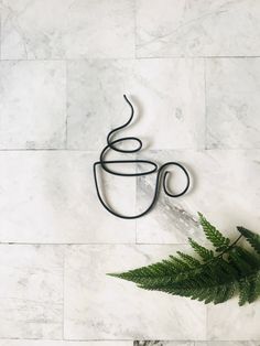 a cup of coffee sitting on top of a white marble counter next to a fern