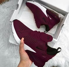 someone is holding up their maroon nike shoes in a box on a white fur rug