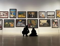 two people sitting on the ground in front of some art