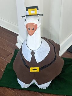 a paper mache duck wearing a pilgrim hat and brown outfit on a green mat