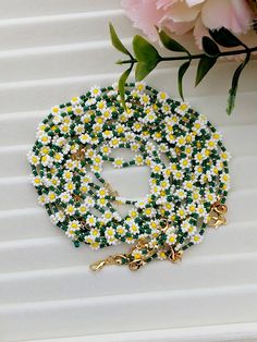 a necklace with daisies on it next to a flower bouquet and a pink rose