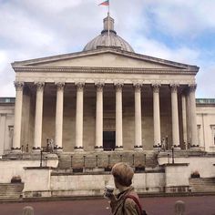 a person standing in front of a building with columns and a flag on the roof