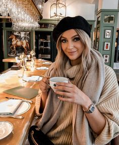 a woman sitting at a table holding a cup