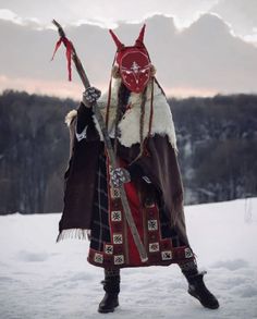 a man dressed in costume holding a stick and wearing a horned headdress, standing in the snow