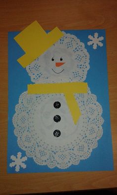 a snowman made out of paper on top of a wooden table with white doily