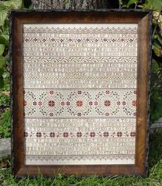 a wooden frame with a pattern on it in the grass next to a tree and bushes