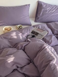 an unmade bed with purple comforter and pillows on top of it, next to a bowl of cereal