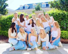 a group of women sitting next to each other in front of a house and bushes