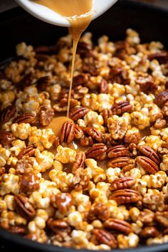 caramel being drizzled over popcorn in a skillet with nuts and pecans