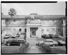 an old black and white photo of cars parked in front of a building with palm trees