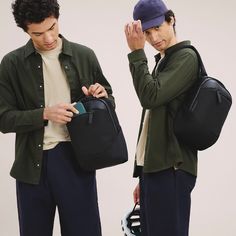 two young men standing next to each other with backpacks on their backs and one holding a cell phone