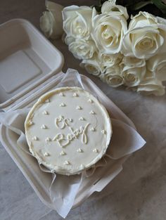 a white cake in a box next to some flowers