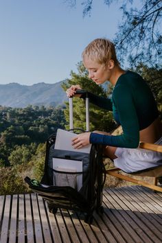 a woman sitting on a chair holding a suitcase and looking at the mountains in the distance