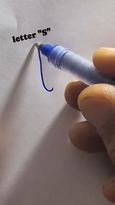 a hand holding a pen over a piece of paper with the letter s on it