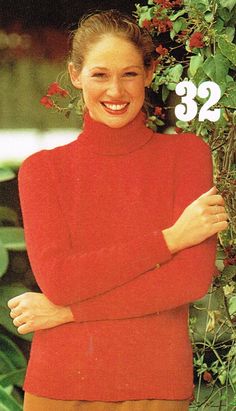 a woman wearing a red turtle neck sweater and tan shorts with her arms crossed, smiling at the camera