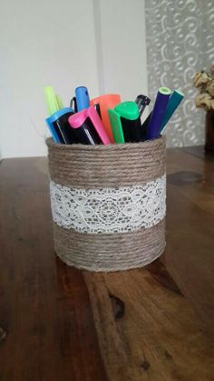 a cup with some pens and markers in it on top of a wooden table next to a vase