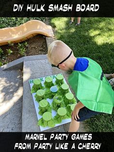 a young boy in green shirt and cape playing with paper plates on sidewalk next to slide