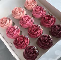 twelve cupcakes with pink frosting in a white box on a gray table