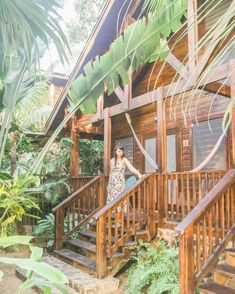 a woman standing on the porch of a wooden house surrounded by greenery and palm trees