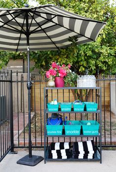 a black and white striped umbrella over a shelf with blue containers on it in front of a fence