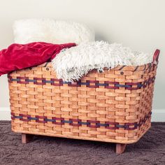 a basket that is sitting on the floor with a red blanket and some white pillows