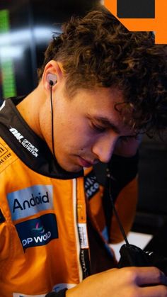 a man with headphones on looking at his cell phone while wearing an orange shirt