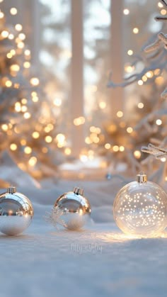 three glass christmas ornaments sitting in front of a white christmas tree with lights on it