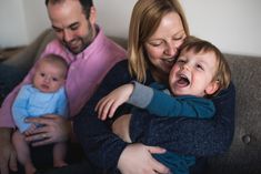 a man and woman holding a baby while sitting on a couch with their arms around each other