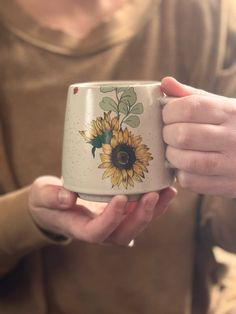 a person holding a coffee mug with a sunflower painted on it