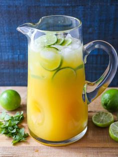 a pitcher filled with lemonade and limes on top of a wooden cutting board