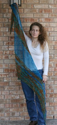 a woman standing next to a brick wall holding onto a blue shawl that is draped over her head