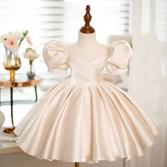 Expertly crafted with a princess silhouette and short puff sleeves, this tea length flower girl dress is perfect for any special occasion. Made from satin fabric in a beautiful champagne color, it features a back zip and bow/tie back for a chic and elegant look. Ideal for weddings, communions, and more.