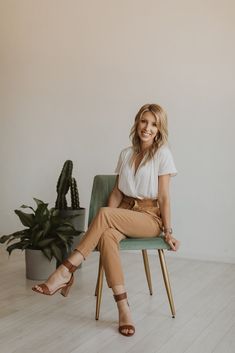 a woman is sitting on a chair in front of a potted plant and smiling