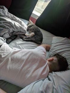 a man laying in bed next to a cat on top of his back and sleeping