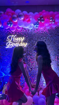 two women in red dresses standing next to each other with balloons and lights behind them