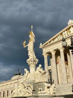 a statue in front of a large building with columns and statues on the sides under a cloudy sky