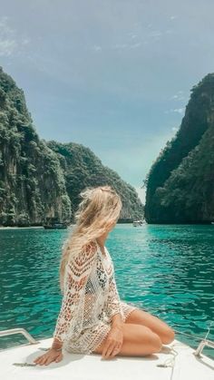 a woman is sitting on the bow of a boat in front of mountains and blue water