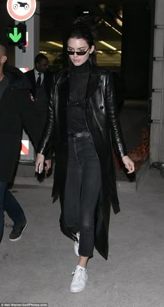 a woman in black jacket and jeans walking through an airport