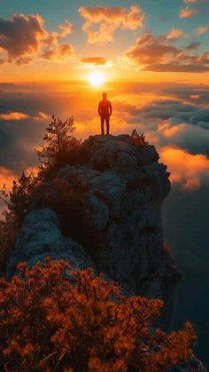 a man standing on top of a mountain with the sun setting behind him and clouds in the sky