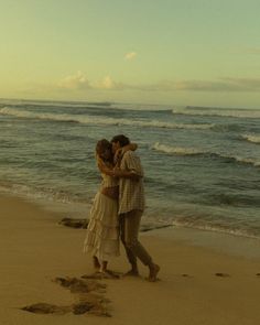 two people are hugging on the beach by the water